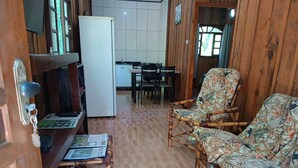 Una habitación con piso de madera, una mesa de comedor con sillas, un refrigerador y dos sillones estampados.
