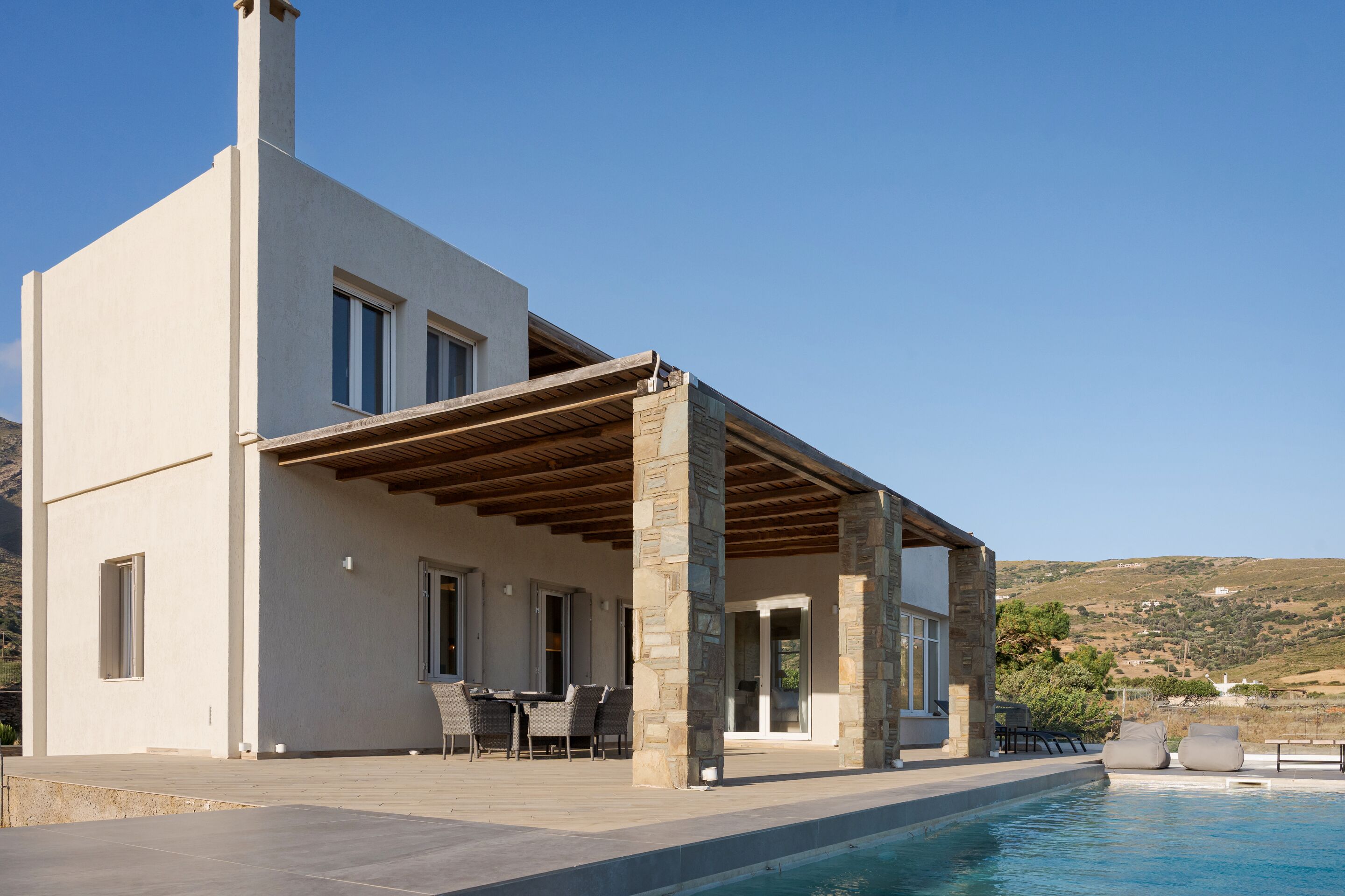 A modern house with a pool, stone pillars, and a covered patio with outdoor furniture.