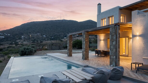 A modern house with a pool, outdoor seating, and a view of the hills. - Andros Royal Villa (Koumari)