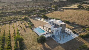 A modern house with a swimming pool, surrounded by fields and a hilly landscape. - Andros Royal Villa (Koumari)