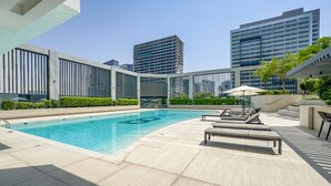 A rooftop pool with lounge chairs and a view of surrounding high-rise buildings. - Stylish Top-Floor 1BR with City Views, Close to Dubai Water Canal (Dubai)