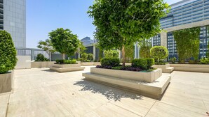 A modern outdoor courtyard with geometric planters and trees, surrounded by high-rise buildings. - Stylish Top-Floor 1BR with City Views, Close to Dubai Water Canal (Dubai)