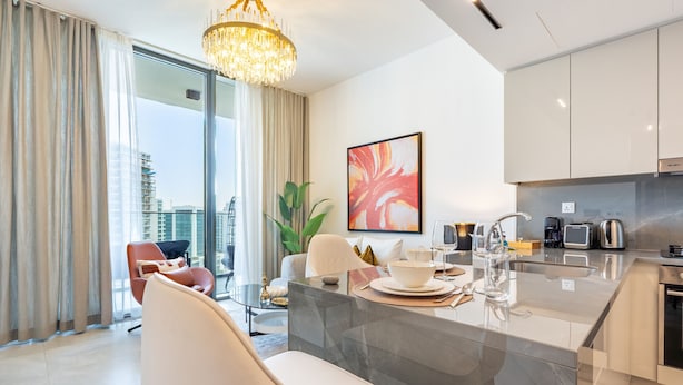 A modern kitchen with a glass island, white cabinetry, and a view of the city. - Stylish Top-Floor 1BR with City Views, Close to Dubai Water Canal (Dubai)