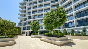 A modern multi-story building with a courtyard featuring planters and trees. - Stylish Top-Floor 1BR with City Views, Close to Dubai Water Canal (Dubai)