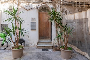 A building entrance with a wooden door, potted plants, a bicycle, and a sign. - Marzapane apartment near Porta Carini (PALERMO)