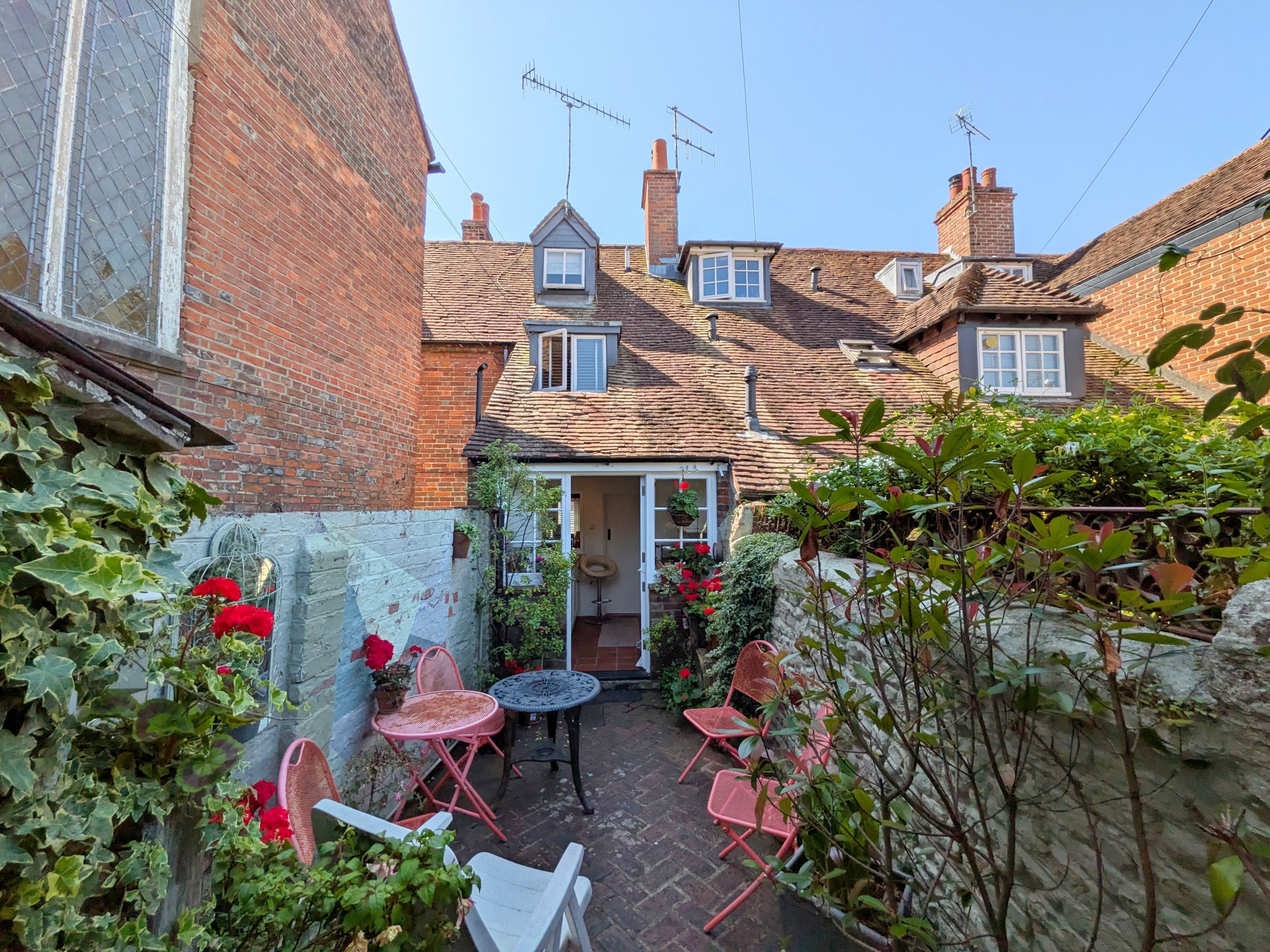 A courtyard with brick walls, a small garden, and a traditional house with a tiled roof.