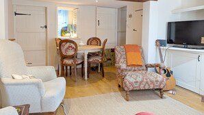 En stue med sofa, en lænestol med mønster, et spisebord med stole, et fjernsyn og en guitar.