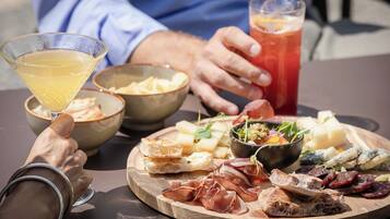 Une table garnie d’une variété d’aliments, notamment du fromage, de la charcuterie et du pain, ainsi qu’un verre à martini et un verre d’une boisson rouge.