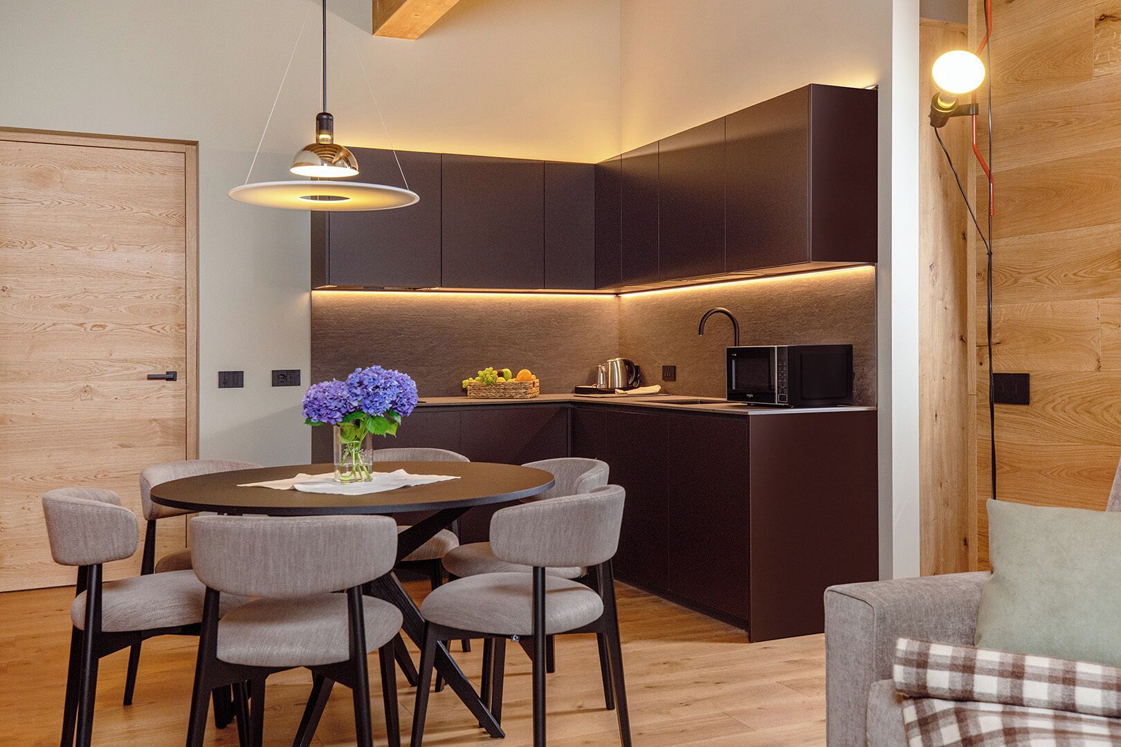 Una cocina moderna con armarios oscuros, un microondas integrado y un comedor con una mesa redonda y sillas.