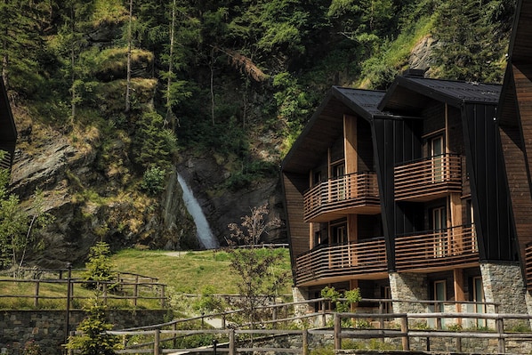 Un edificio de madera de varios pisos con balcones, con un acantilado rocoso y una cascada de fondo.