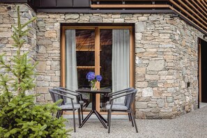 Un edificio de piedra con un ventanal grande, una mesa con sillas y una planta en maceta.