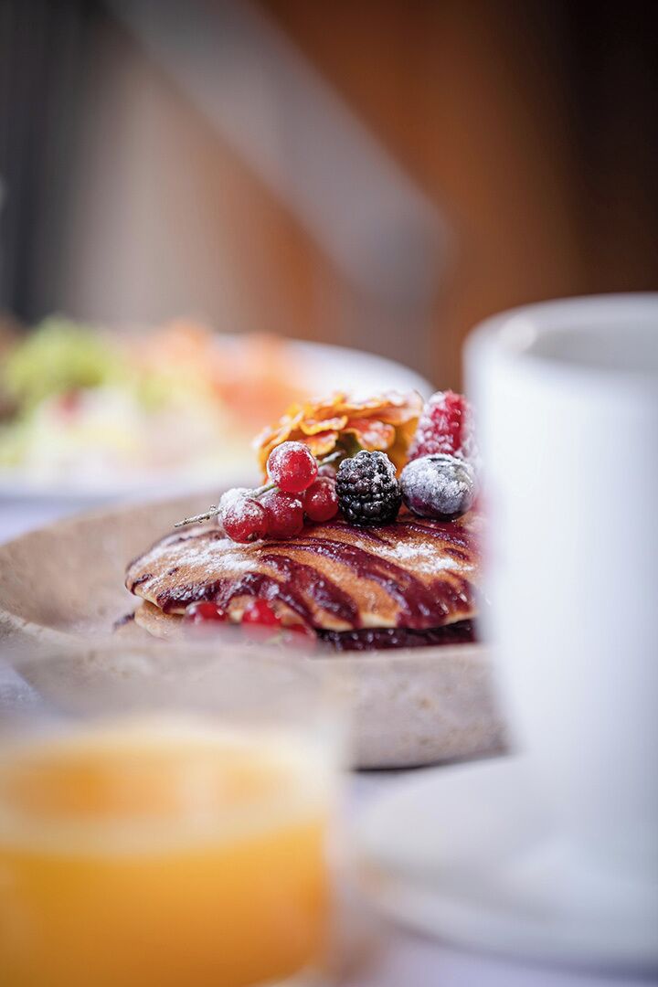 Een ontbijt bord met pannenkoeken, bessen en een glas sinaasappelsap.
