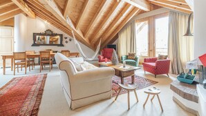A spacious loft with high ceilings, a dining area, and a cozy seating area with a hammock. - Ski-in · Luxury Alpine Apartment · Celerina (Celerina/Schlarigna)