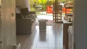 Ein Innenraum mit einer Couch, einem Esstisch und Blick auf einen Garten durch eine Schiebetür.