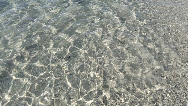 Ein Strand mit klarem, flachen Wasser, einem sandigen Ufer und Bergen in der Ferne.