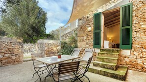 Une terrasse extérieure avec une table et des chaises, des murs en pierre et un escalier menant à un niveau supérieur.