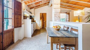 Une cuisine rustique avec des meubles en bois, un pilier en pierre et un coin repas comprenant une table et des chaises.