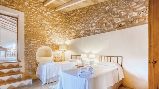 Une chambre avec deux lits, un mur en pierre, une porte en bois et un escalier.
