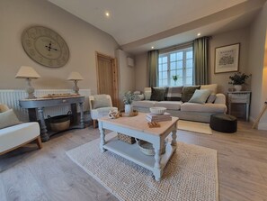 Un salon avec un canapé, une table basse, une horloge et une fenêtre avec des rideaux.