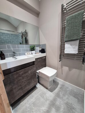 Une salle de bain moderne avec un lavabo blanc, un meuble-lavabo en bois foncé, des toilettes blanches et un porte-serviettes agrémenté d’un tapis vert.