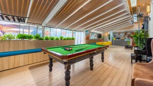 A pool table in a room with wooden flooring, a reception desk, and a seating area with plants. - yipingjuminsu (Shenzhen)