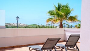 Eine Terrasse mit zwei Liegestühlen, einer Lampe und Blick auf das Meer und die Hügel.