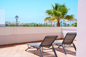 A terrace with two lounge chairs, a lamp, and a view of the sea and hills. - Seaside Light, Praia del Rey (Óbidos)