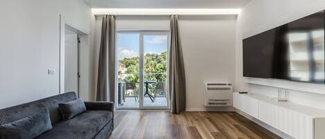 En moderne stue med sofa, et fladskærms-tv, en skydedør til en balkon og et hvidt skab.