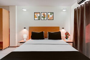 Ein Hotelzimmer mit einem Bett, zwei Nachttischen, einer Wand-Klimaanlage und drei gerahmten Kunstwerken.