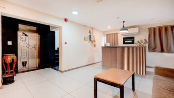 A hotel lobby with a reception desk, a wooden bench, and a staircase leading to an elevator.