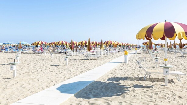 Ein Strand mit Reihen von Liegestühlen und gestreiften Strandsonnenschirmen.