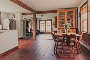 A dining area with a wooden table and chairs, a cabinet with glass doors, and a kitchen area with a refrigerator. - Entire Farm! The Homestead & Barn at Winterfound (Woodstock)