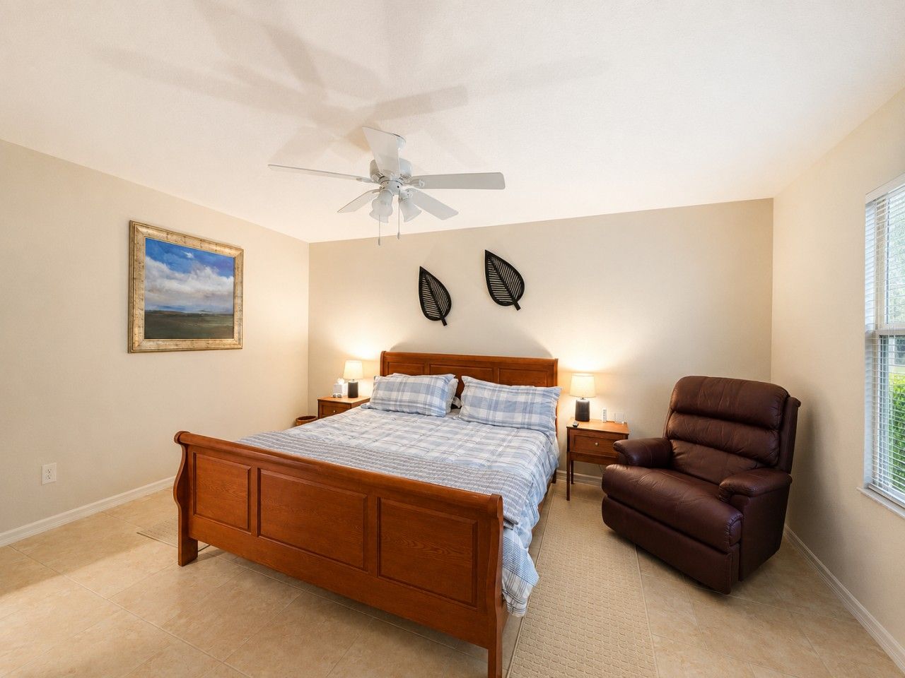 Ein Schlafzimmer mit einem hölzernen Bett, einem Deckenventilator, einem braunen Ledersessel und einem Bild an der Wand.