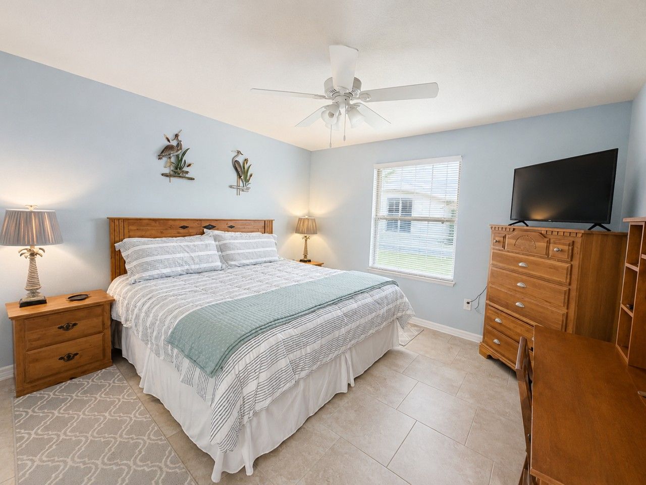 A bedroom with a bed, nightstands, a dresser, a television, a ceiling fan, and a window.