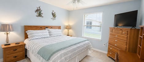 A bedroom with a bed, nightstands, a dresser, a television, a ceiling fan, and a window.
