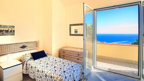 Un dormitorio con cama, mesita de noche, cómoda y balcón con vista al mar.