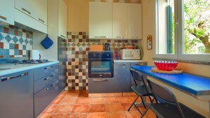 Una cocina compacta con salpicadero de azulejos, estufa, horno, microondas y ventana con vistas a la vegetación.