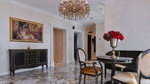 Un vestíbulo con piso de mármol, una araña, un cuadro, un aparador y una mesa con un jarrón de flores.