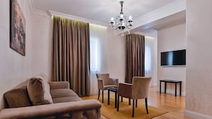 Una sala de estar con un sofá, sillas, una araña, cortinas y un televisor.