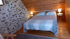 Ein gemütliches Zimmer mit einem Bett, zwei Nachttischlampen, Holzboden, Steinwand und einem kleinen Holzstuhl.