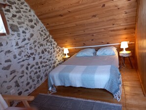 Ett mysigt rum med en säng, två sänglampor, ett trägolv, en vägg av sten och en liten trästol.