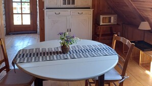 Ein Holzinnenraum mit einem runden Tisch, Stühlen, einer Pendelleuchte, einem Schrank und einer Tür, die nach draußen führt.