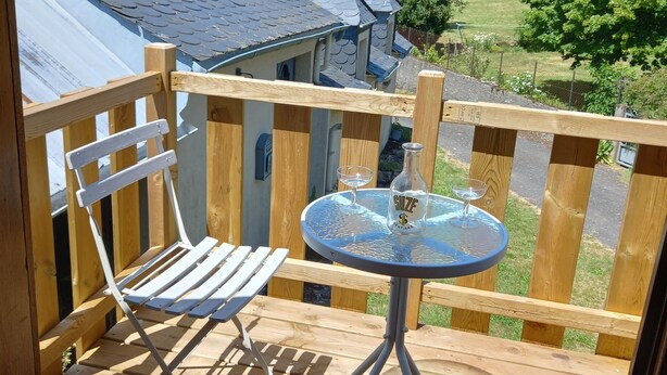 Eine Holzterrasse mit einem tischgestellten Metalltisch und einem weißen Stuhl, mit Blick auf eine Wohngegend mit Häusern und Bäumen.