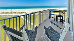 A balcony with a view of the beach, a table, and two chairs. - Estero Beach & Tennis 303B | Beachfront Studio + Resort Amenities (Fort Myers Beach)