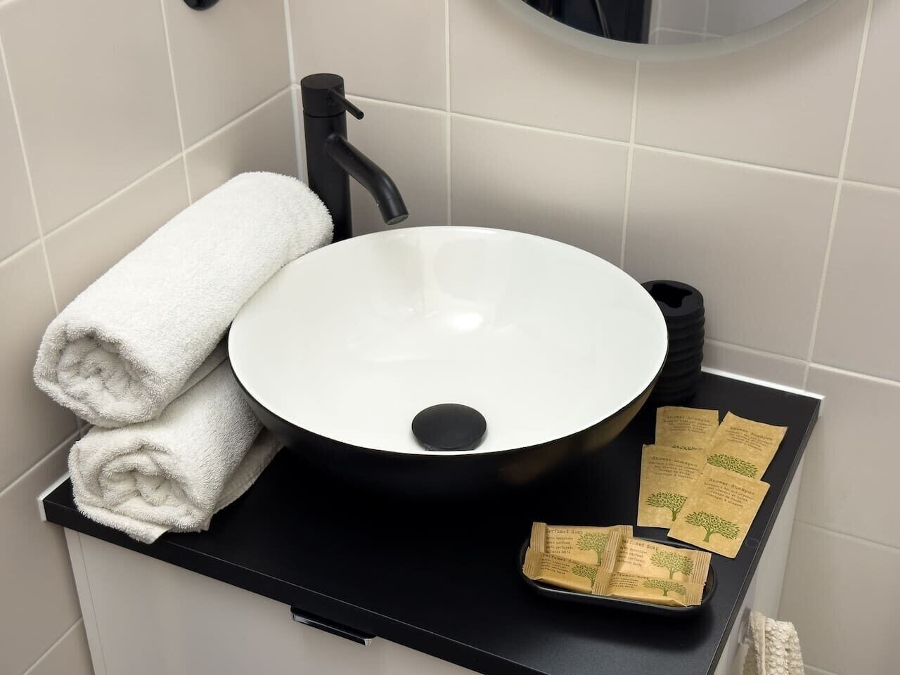 A bathroom with a white sink, black faucet, and towels on a black countertop.