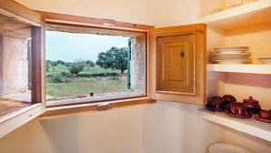 Una cocina con ventana, armarios de madera y estante con platos y teteras.
