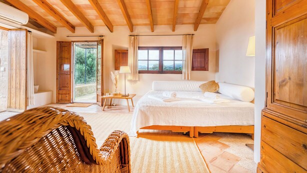 Un dormitorio con techo de madera, una cama grande, una silla de mimbre y vistas al exterior.
