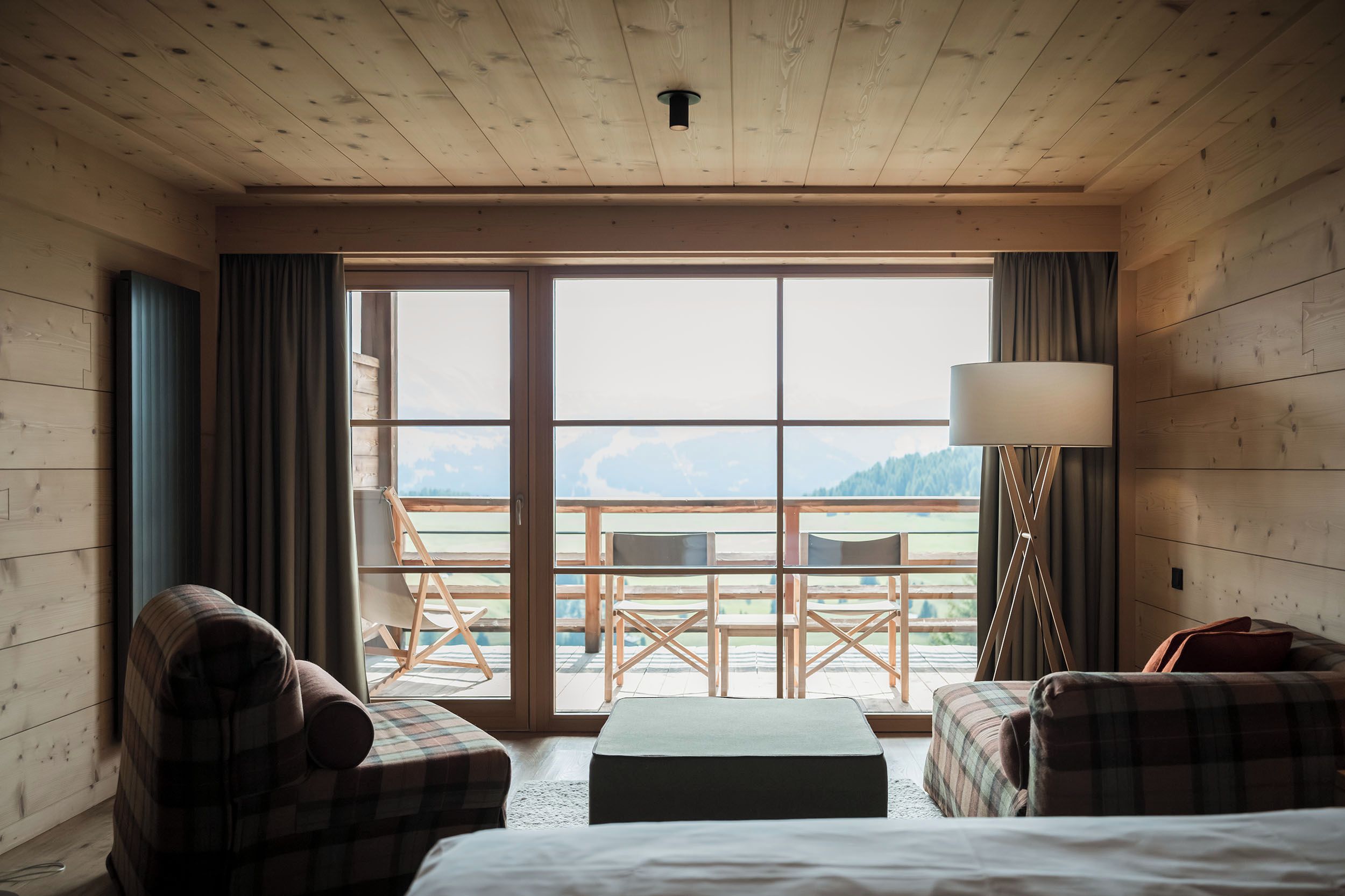A hotel room with a large sliding glass door leading to an outdoor terrace with a view of the mountains.