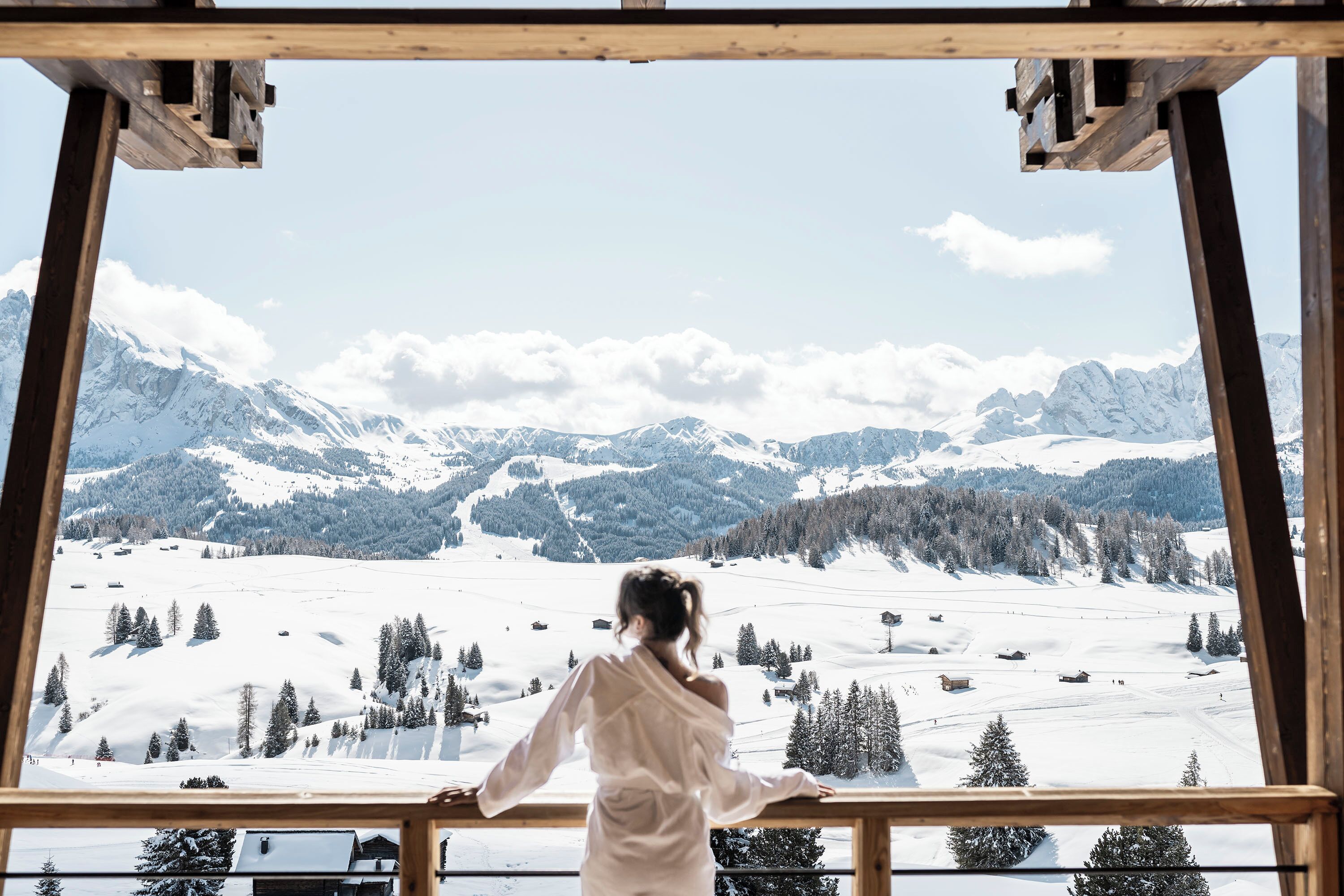 Una persona de pie junto a una ventana con vistas a un paisaje montañoso nevado.