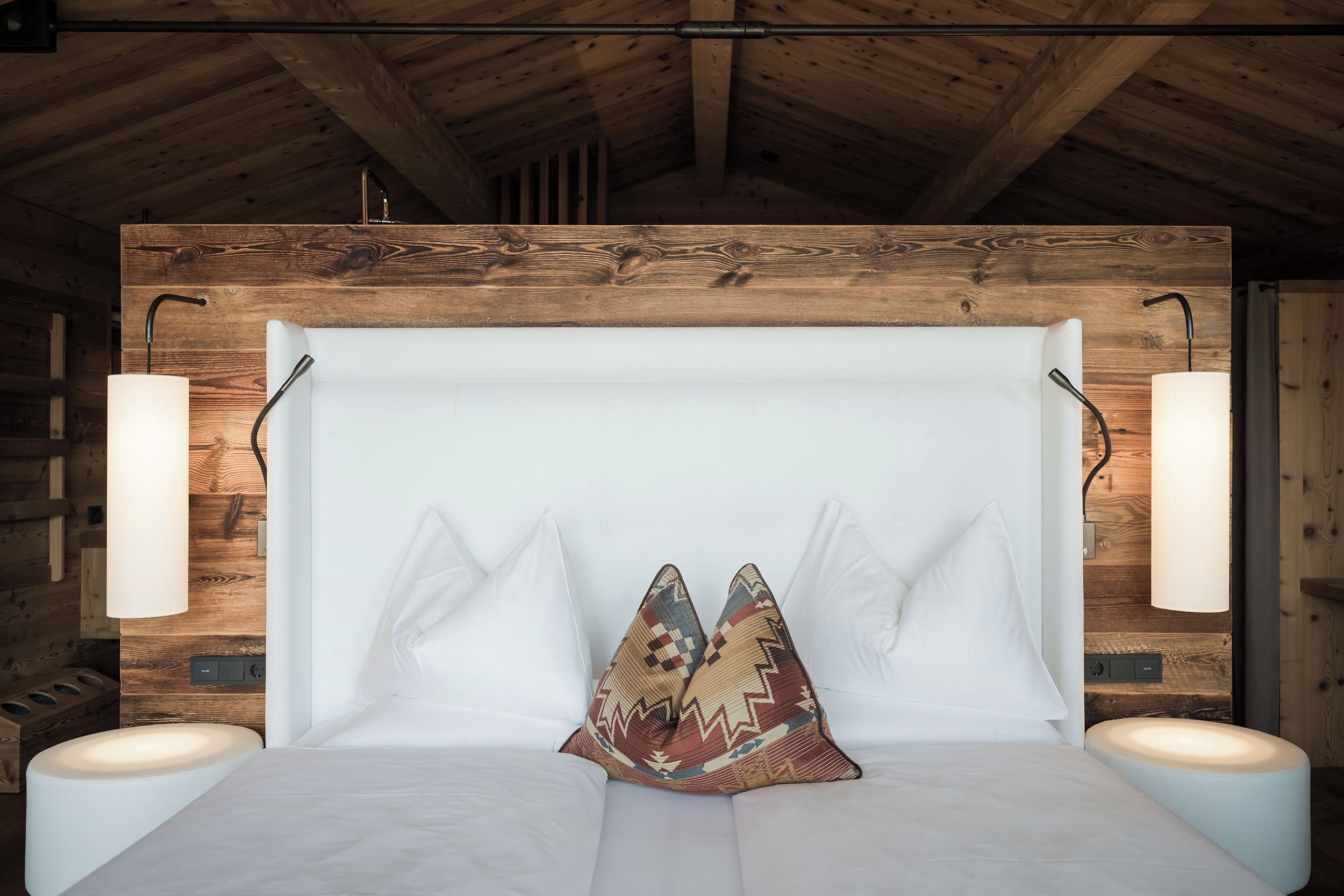 Ein Zimmer mit Holzboden, einem Bett mit weißer Bettwäsche, zwei Nachttischlampen und einem gemusterten Kissen.